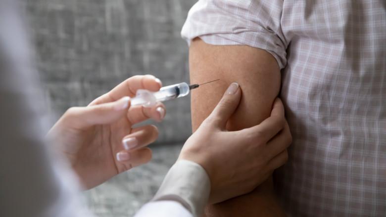 Hoitaja rokottaa vanhemman miehen käsivartta.