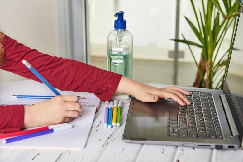 Koulutyttö kirjoittaa kynällä paperille ja käyttää kannettavaa tietokonetta.