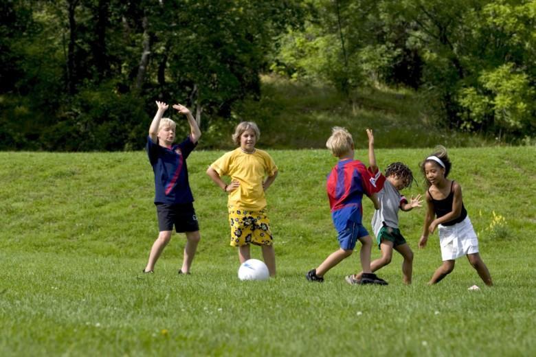 Lapset pelaavat jalkapalloa kesällä ulkona nurmikentällä