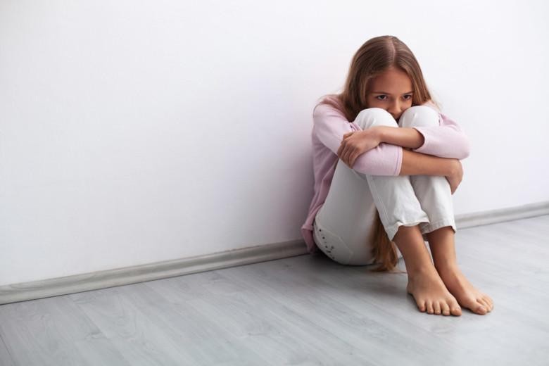 Nuori tyttö istuu yksin seinän vieressä lattialla huolissaan.