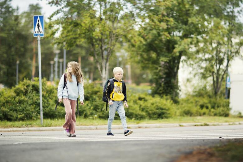 Kaksi lasta koulureput selässään ylittää suojatietä.